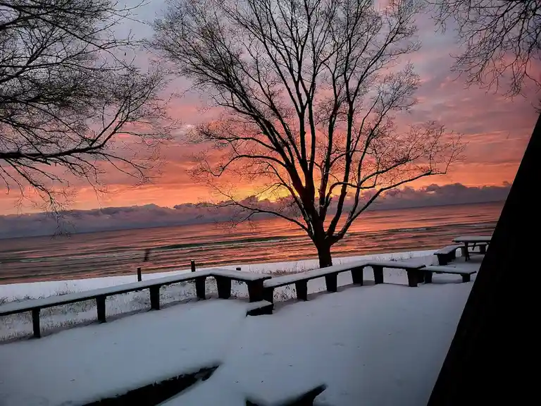 A serene winter sunset over a snow-covered beach with bare trees and wooden benches, overlaid with the text 'i'm not lazy…