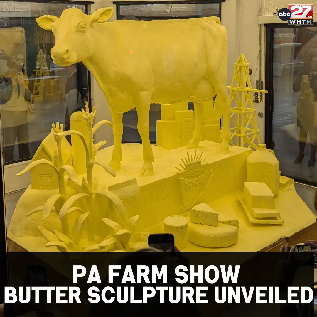 A large, detailed butter sculpture at a Pennsylvania Farm Show features a prominent yellow cow standing atop a diorama with…