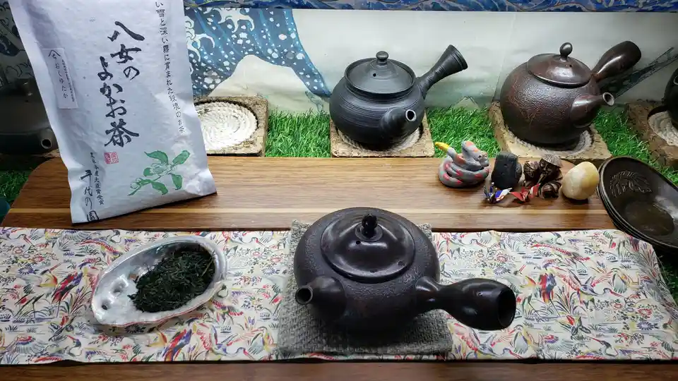A still life of traditional Japanese tea ceremony items including three ceramic teapots, a bag of green tea labeled…