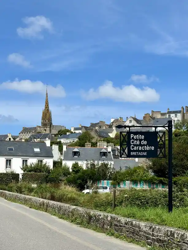 A scenic photo of a quaint French village with traditional stone houses and a prominent church spire under a blue sky…