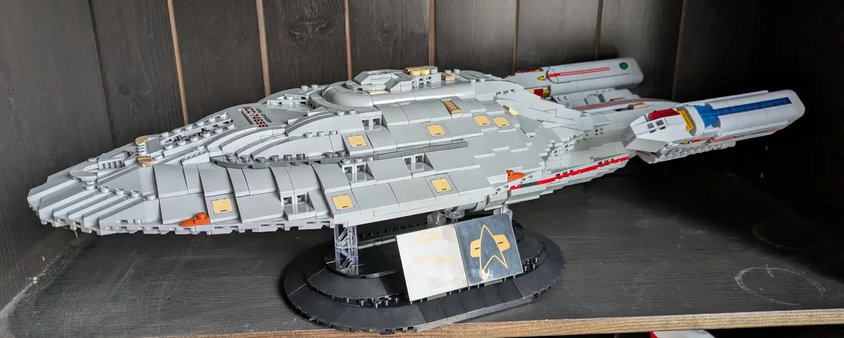A detailed LEGO model of the Star Trek Voyager starship, marked with 'NCC-74656', is displayed on a black circular stand…