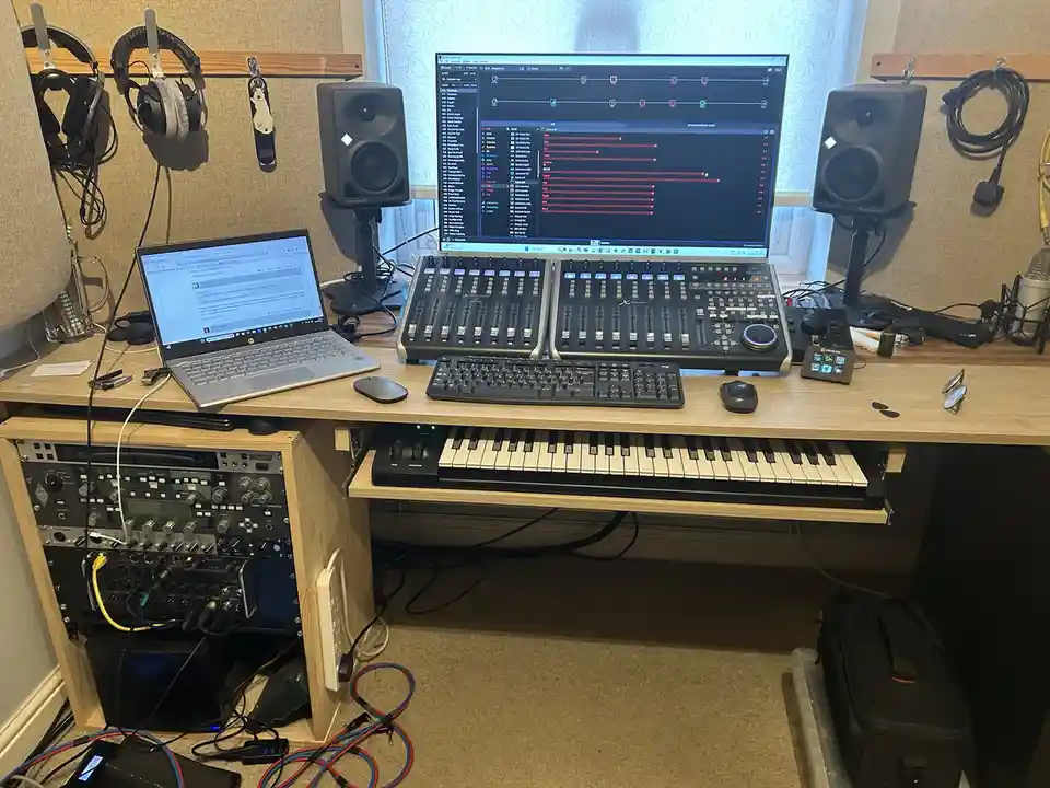 A professional music production setup with a large monitor displaying a digital audio workstation with red audio waveforms…