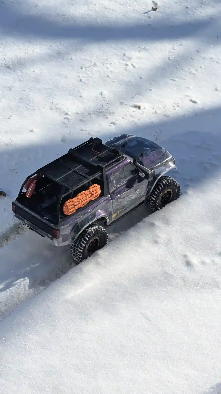 A heavily modified remote-controlled pickup truck with a purple glitter paint job, black roof rack, and orange toolbox sits…