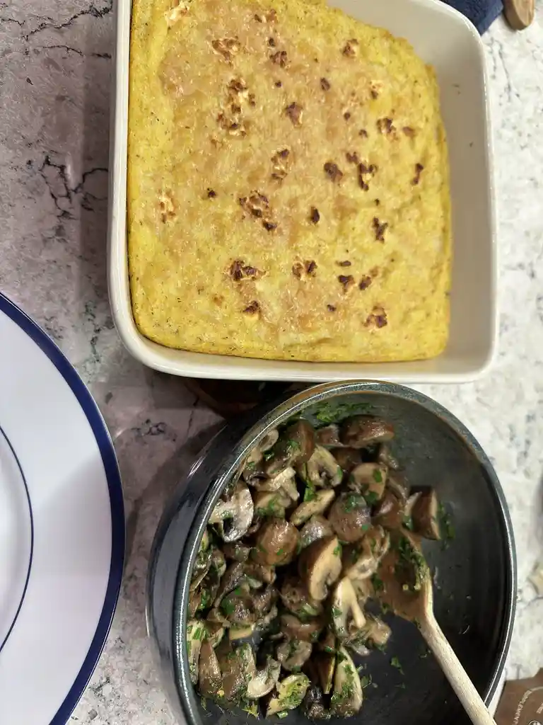 A top-down photo shows a white rectangular baking dish containing a golden-brown, slightly crispy casserole, next to a dark…