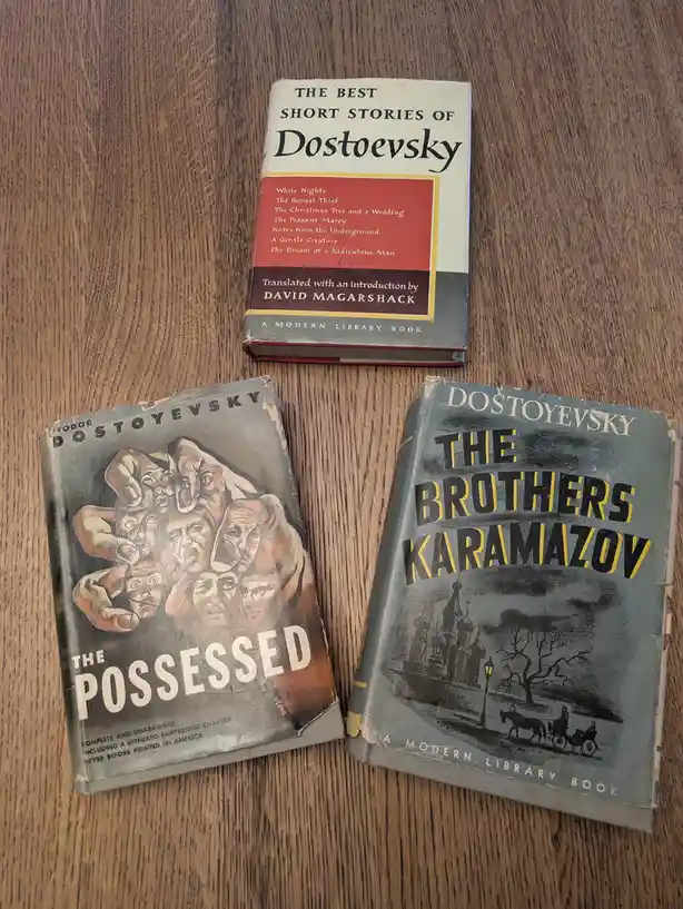 Three vintage Dostoevsky books lie on a wooden surface: 'The Best Short Stories of Dostoevsky' at the top, with 'The…