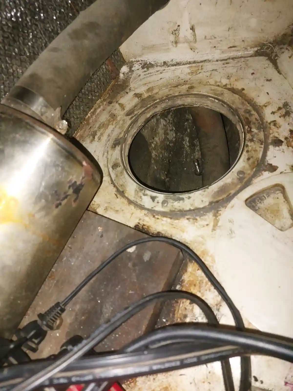 A close-up photo shows a dirty, grimy circular opening in a white, stained surface, likely a fuel tank or similar container…