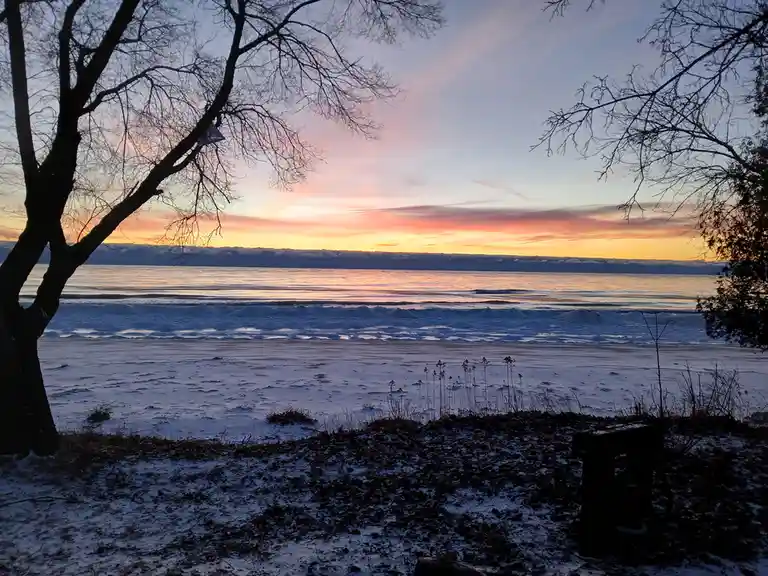 A serene winter sunset over a frozen beach with bare trees framing the view, overlaid with the text 'i'm not crying, you're…