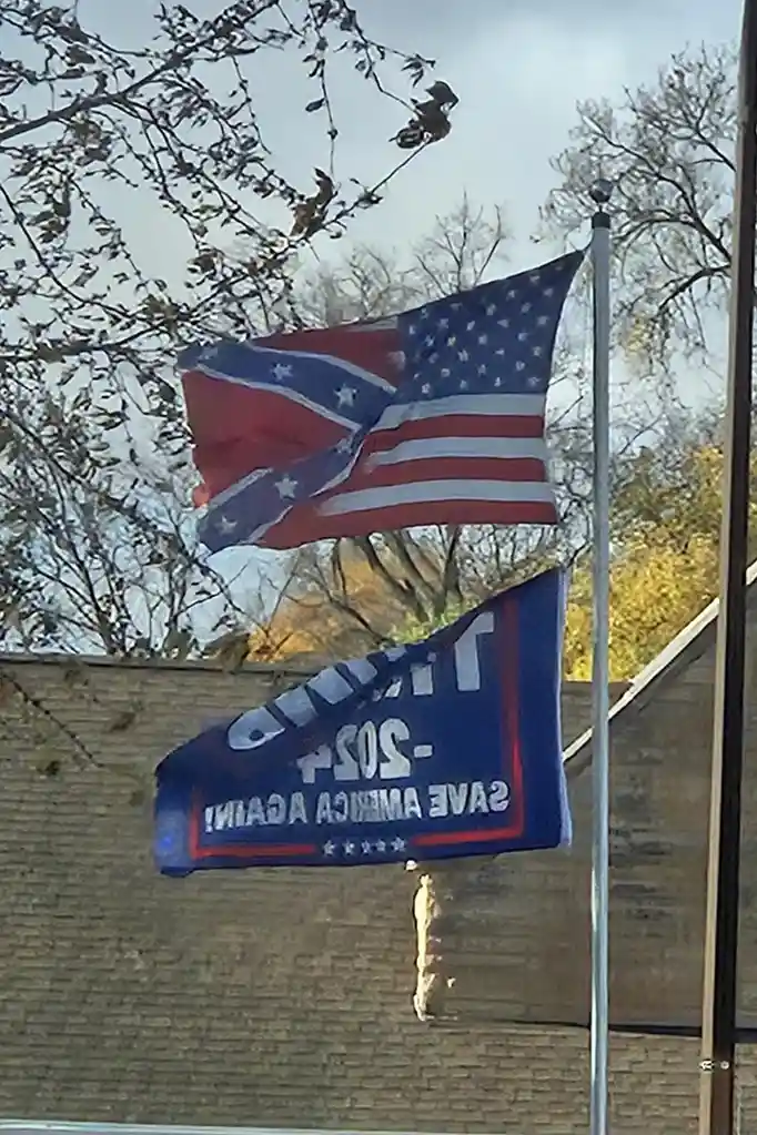 An American flag is visibly altered to include a Confederate battle flag design in its canton, flying on a pole against a…