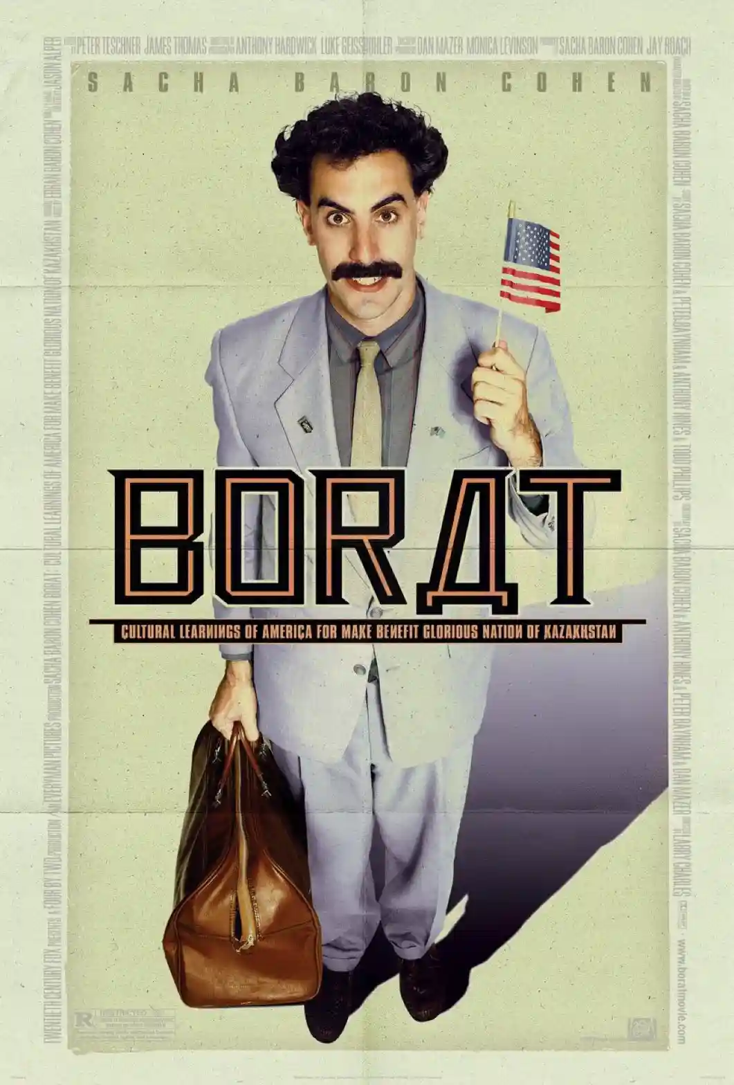 A movie poster for 'Borat' shows actor Sacha Baron Cohen as the titular character, wearing a light gray suit, holding a…