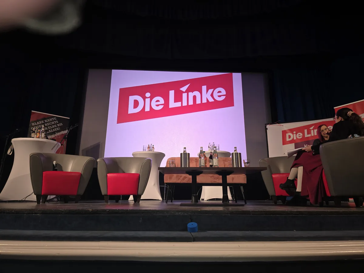 A stage setup for a political event featuring the German left-wing party 'Die Linke', with multiple armchairs, a central…