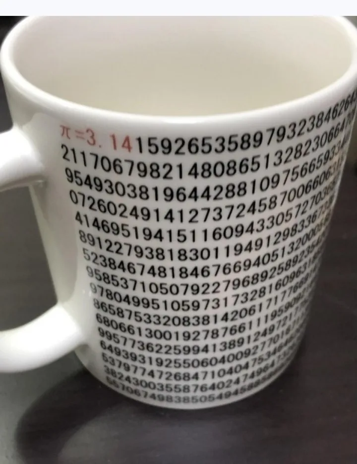 A white ceramic mug displays the mathematical constant pi (π) incorrectly stated as equal to 3, followed by a long sequence…