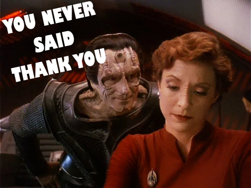 A still from Star Trek: The Next Generation shows a Klingon character leaning in menacingly behind a human woman in a red…