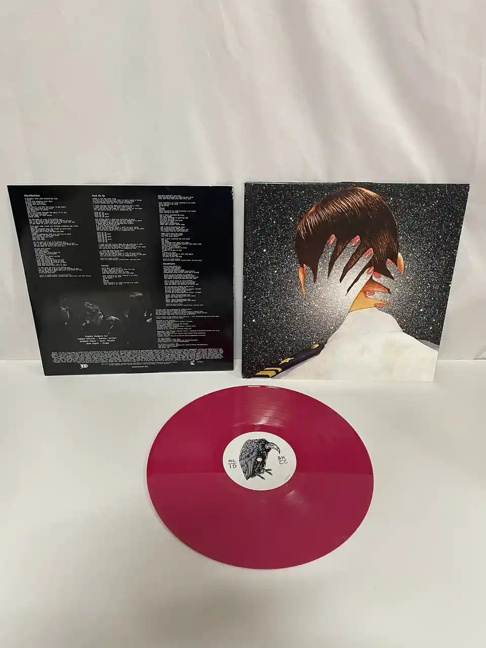 A red vinyl record sits in front of its album cover and inner sleeve. The cover art shows a person from behind with glittery…