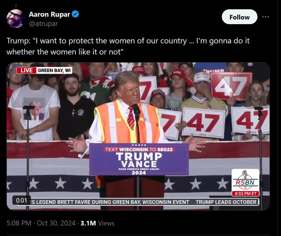 A screenshot of Donald Trump speaking at a rally in Green Bay, Wisconsin, wearing an orange safety vest over his suit…