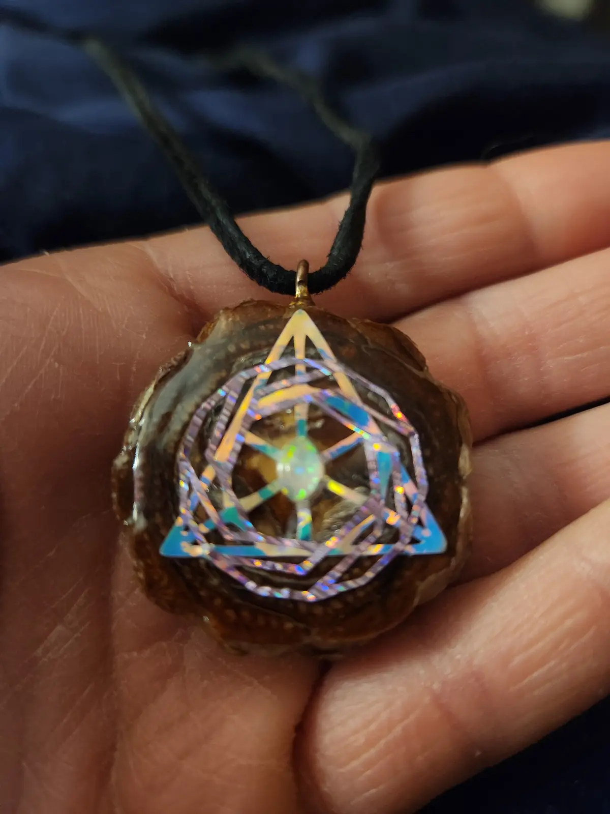 A hand holds a pendant made from a brown, irregularly shaped natural stone, suspended from a black cord. The stone has a…