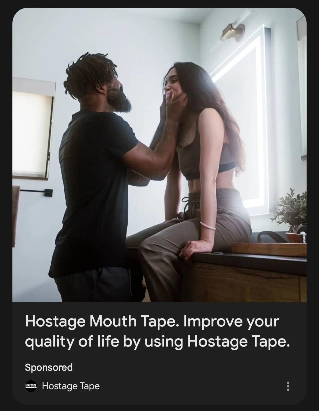 A man in a black t-shirt is holding a woman's face with both hands while she sits on a wooden counter in a bright room. The…