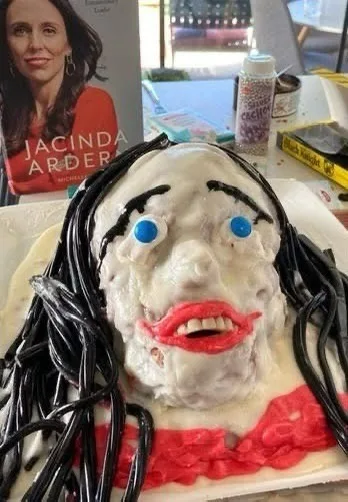 A cake shaped and decorated to resemble a person's face, with black icing hair, blue icing eyes, and red icing lips, placed…