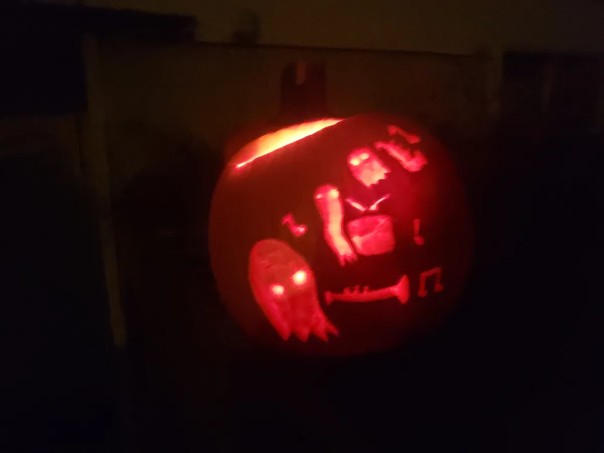 A carved pumpkin illuminated from within, casting a red glow, features silhouettes of ghosts playing musical instruments…