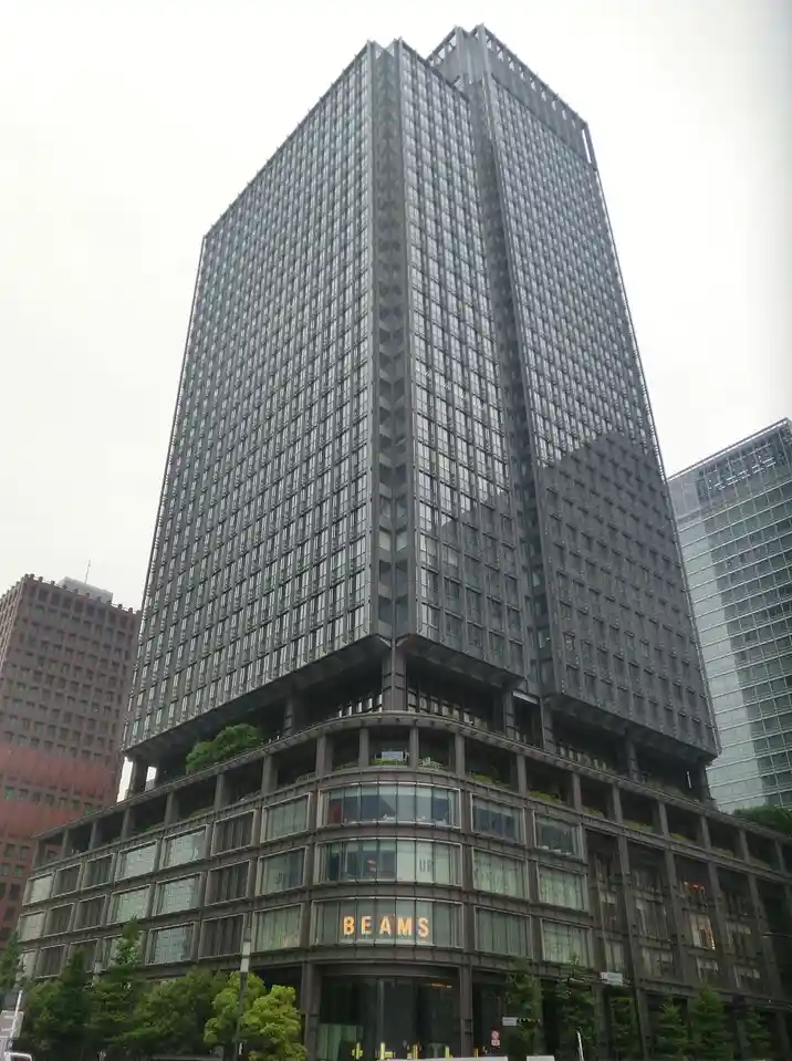 A tall, modern skyscraper with a glass and steel facade, featuring the word 'BEAMS' illuminated in orange letters on its…