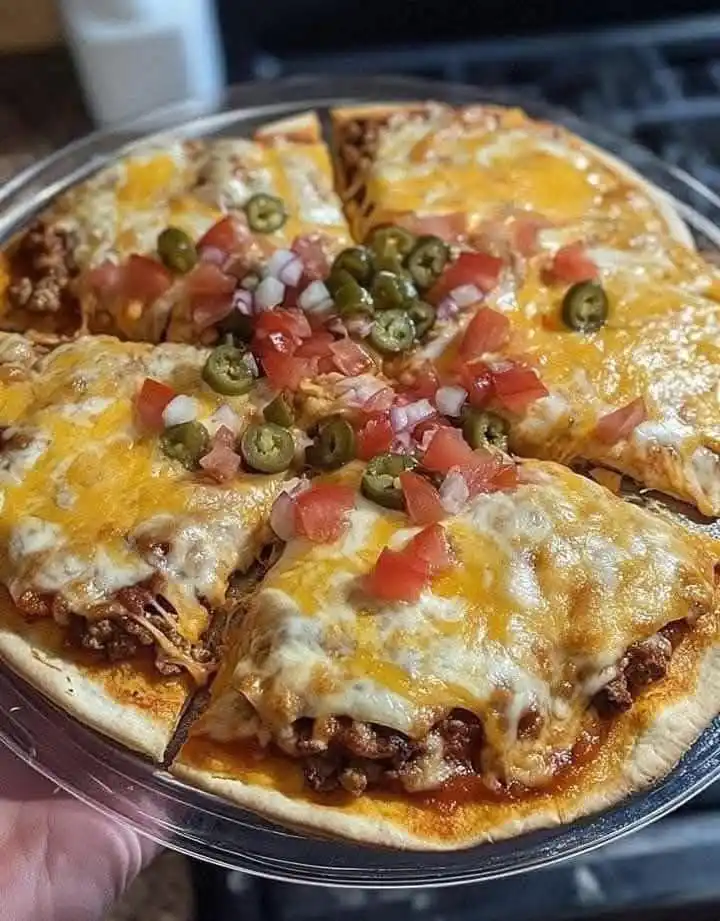 A close-up photo shows a round, sliced dish in a clear glass pie dish, held by a hand. The dish has a crust, melted cheese…