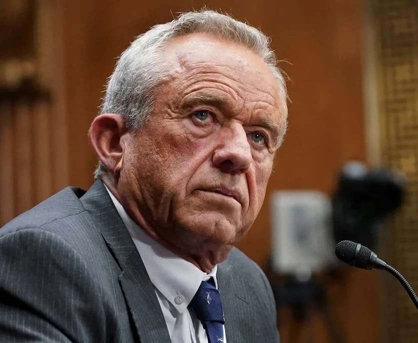 a close-up photo of an older white man with gray hair, wearing a gray suit and blue tie, looking intensely at the camera…
