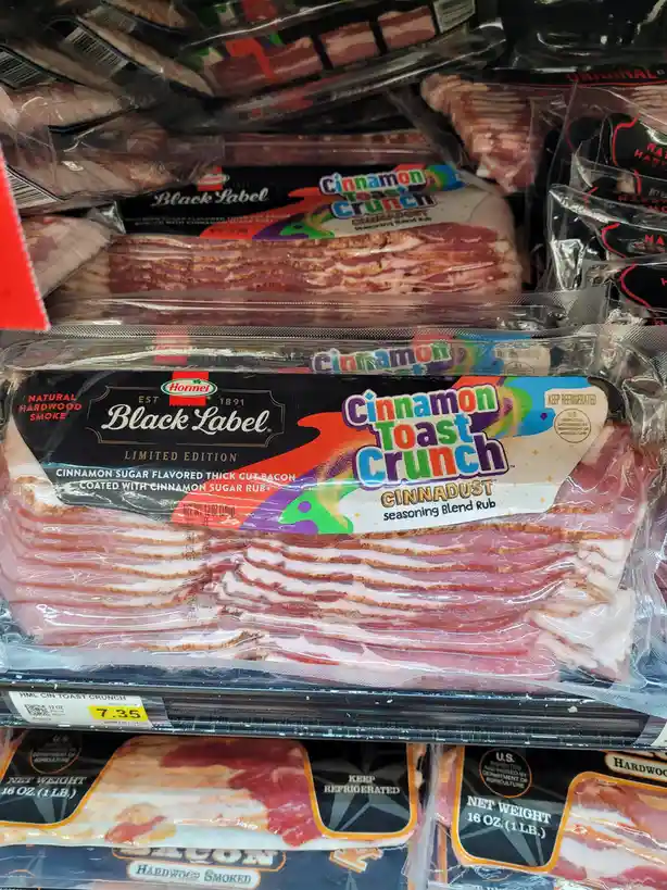 A close-up shot of a package of Hormel Black Label bacon in a grocery store, prominently labeled 'Cinnamon Toast Crunch'…