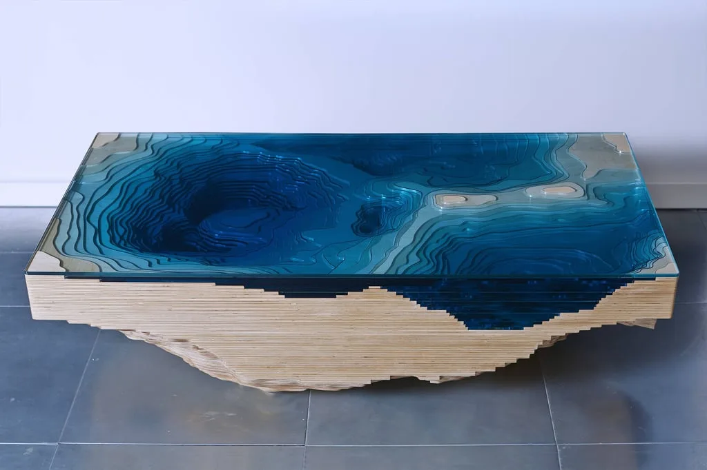 a modern coffee table with a glass top featuring a 3d topographic map of the ocean floor in shades of blue, set on a wooden…