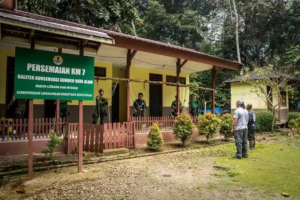 A green sign in front of a yellow building reads 'PERSEMAIAN KM 7 BALITEK KONSERVASI SUMBER DAYA ALAM BADAN LITBANG DAN…