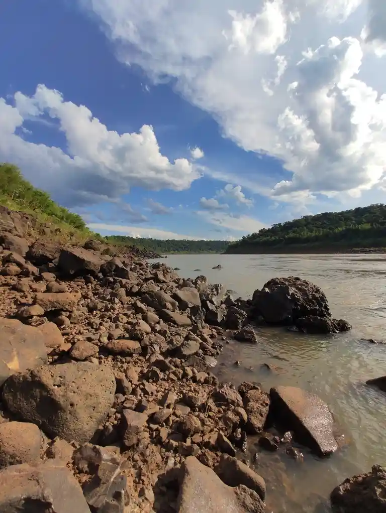 A scenic photo of a riverbank with large rocks and shallow water under a partly cloudy blue sky, overlaid with the text 'i'm…