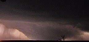 A dark, ominous sky with a massive, glowing storm cloud formation on the horizon, silhouetting a lone, bare tree in the…