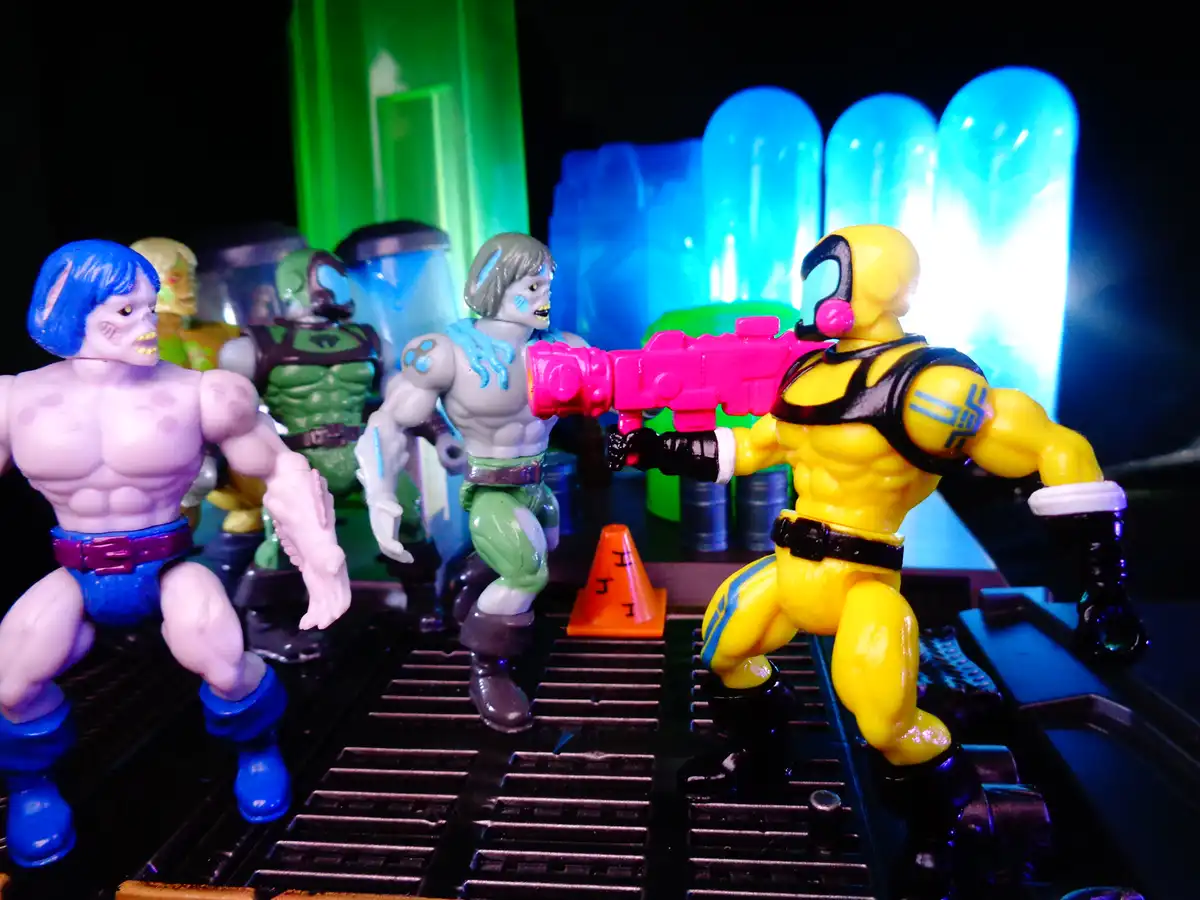 A yellow action figure with a pink gun points at a group of other action figures in a sci-fi setting with glowing blue and…