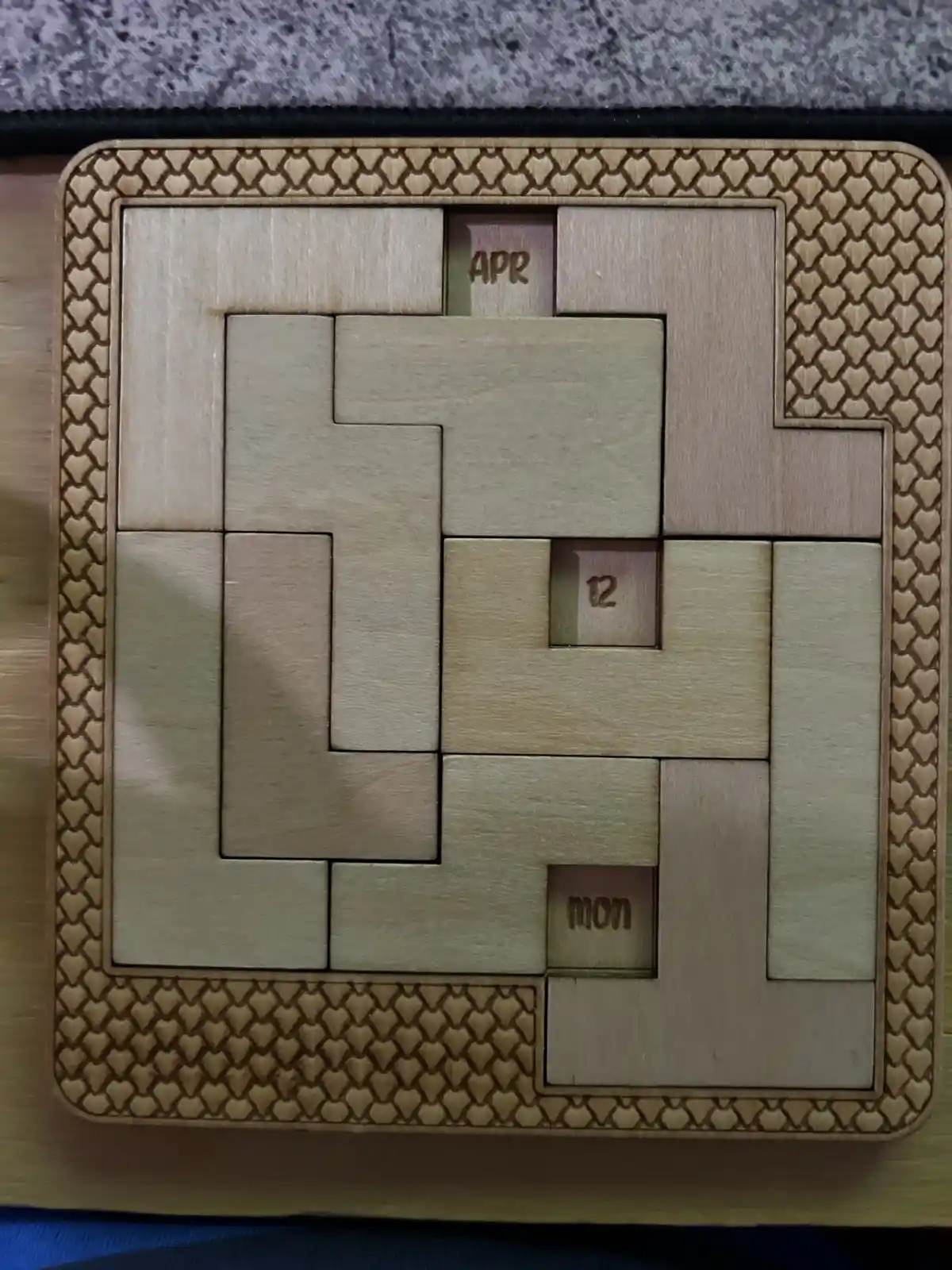 A wooden calendar puzzle with interlocking pieces, showing 'APR' at the top, '12' in the center, and 'mon' at the bottom…