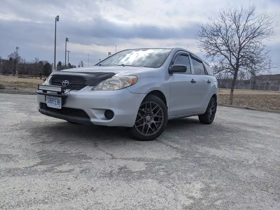 A silver Toyota RAV4 is parked in an outdoor lot with a custom black hood and aftermarket wheels. The Ontario license plate…