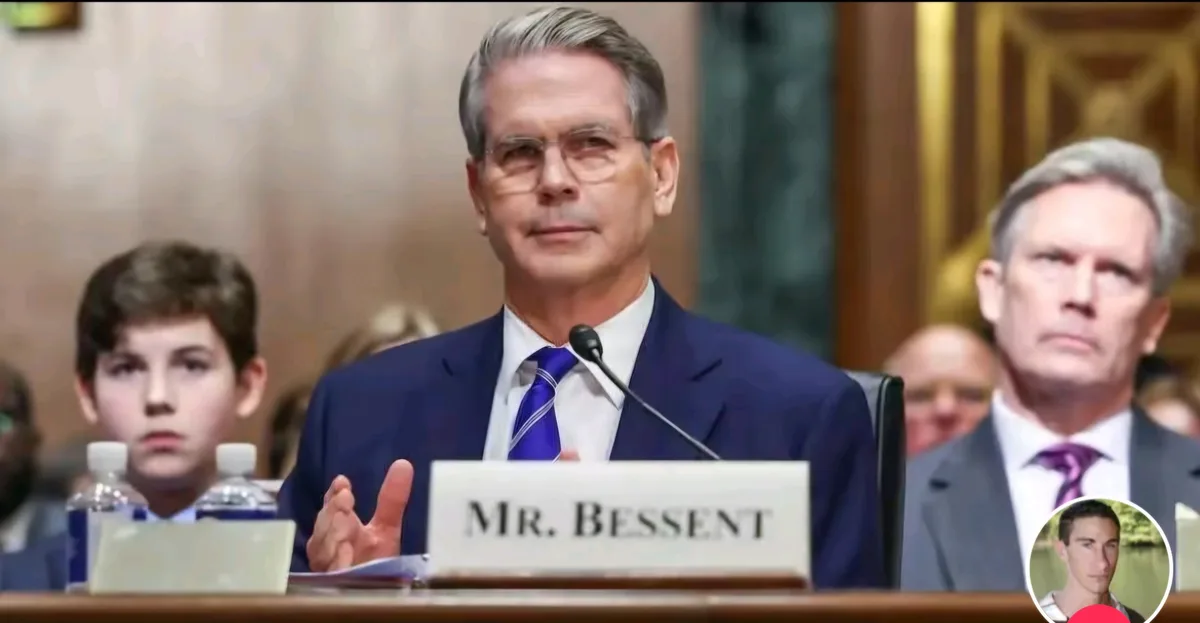 A man in a blue suit and glasses sits at a formal hearing table with a nameplate reading 'MR. BESSSENT', gesturing while…