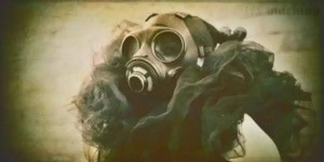 A sepia-toned, grainy image shows a person with long, dark, flowing hair wearing a vintage gas mask. The mask covers the…