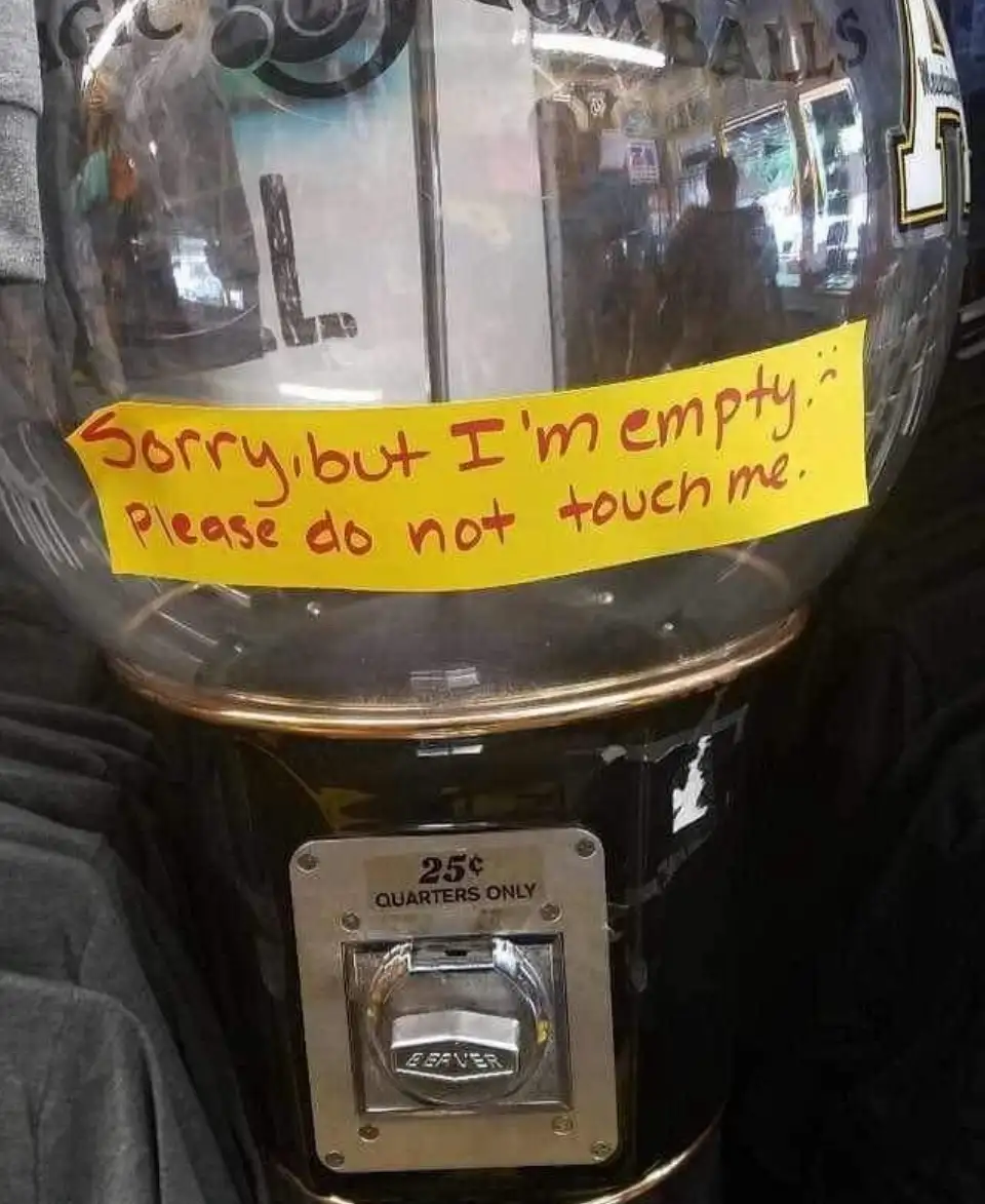 A close-up of an empty gumball machine with a yellow handwritten note taped to its glass globe. The note reads 'Sorry, but…