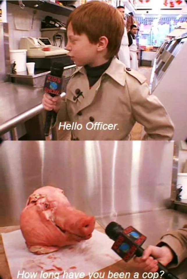 A young boy in a beige trench coat holds a microphone labeled 'KIDS SHOW' and addresses a pig's head on a butcher block…