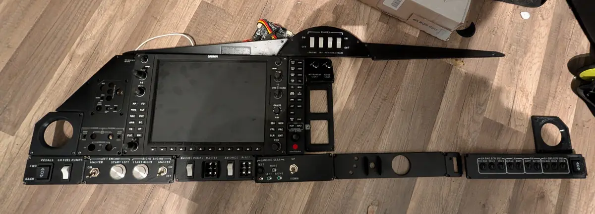 A disassembled airplane cockpit control panel, featuring a central Garmin avionics screen, numerous switches, knobs, and…