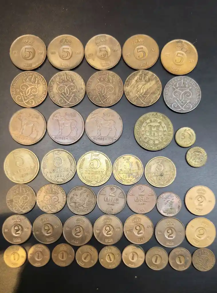 An overhead shot displays a large collection of various old coins from different countries, including Norwegian 5 and 2 ore…