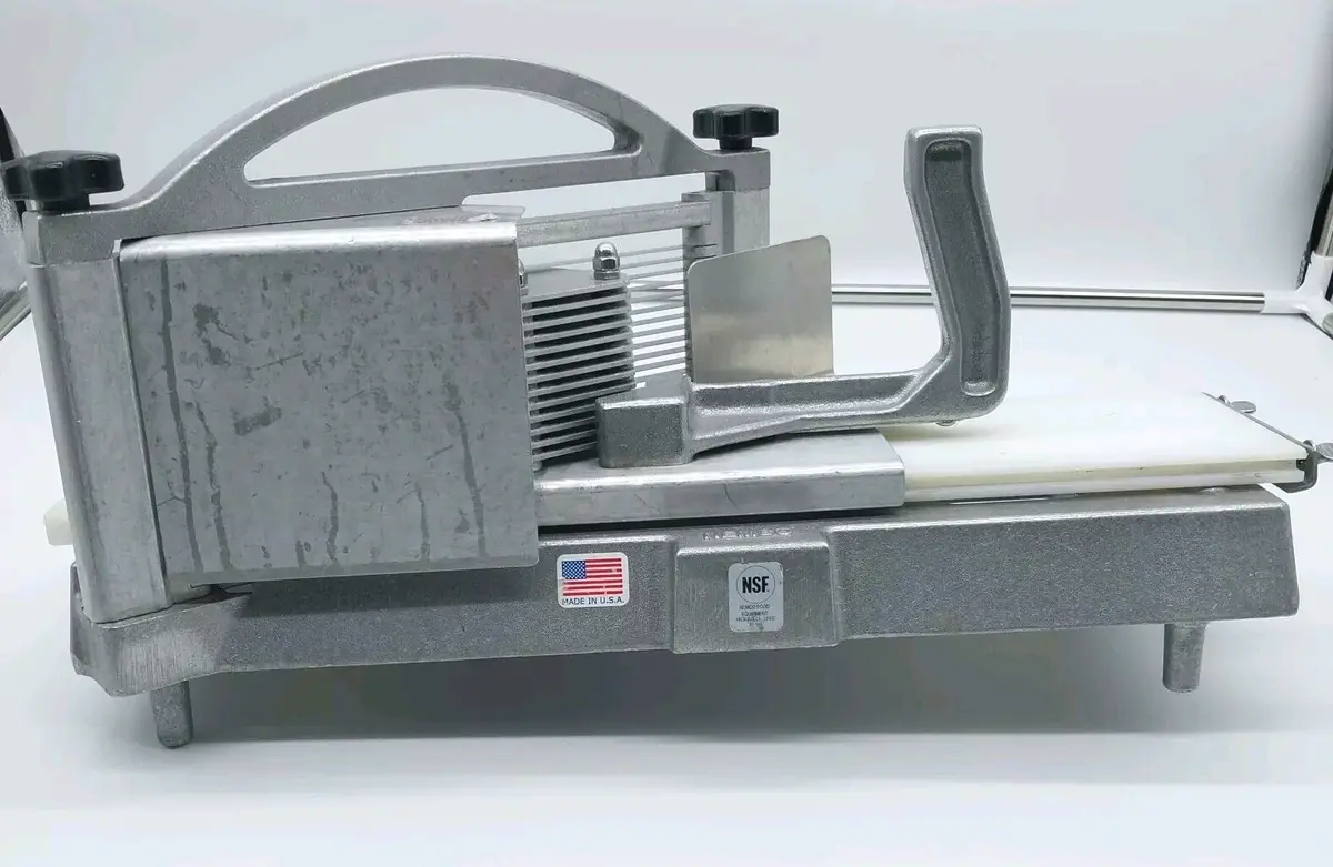 A silver manual meat slicer with a white cutting board, featuring an American flag sticker and an NSF certification label…