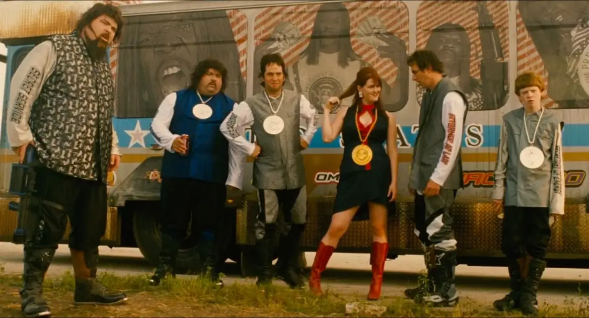 Six people stand in front of a decorated truck, each wearing a white circular medal except one woman in a black dress and…
