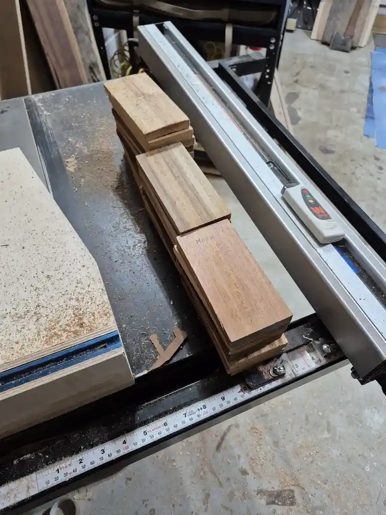 A woodworking scene shows stacks of wooden planks on a table saw, with sawdust scattered around. The overlaid text reads…