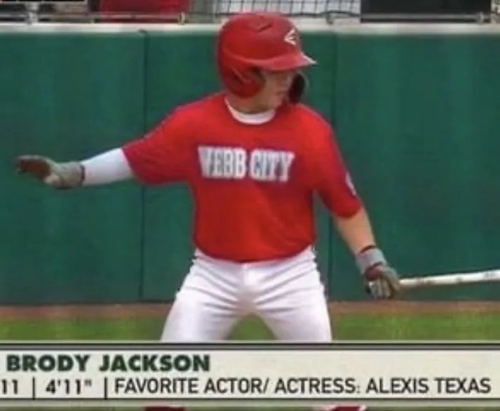 A young baseball player in a red 'WEBB CITY' jersey and helmet stands at bat, holding a bat and gesturing with his left…