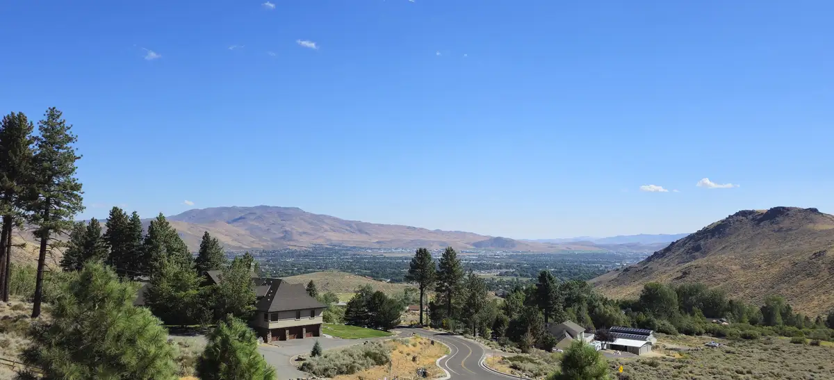 A scenic photo shows a house perched on a hillside overlooking a sprawling valley with distant mountains under a clear blue…