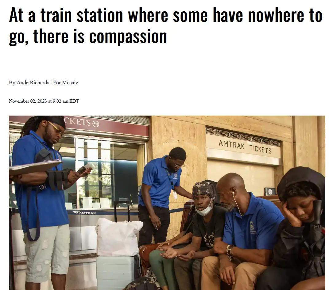 The image shows several Black men in a train station, some sitting on benches with luggage, while two in blue shirts appear…
