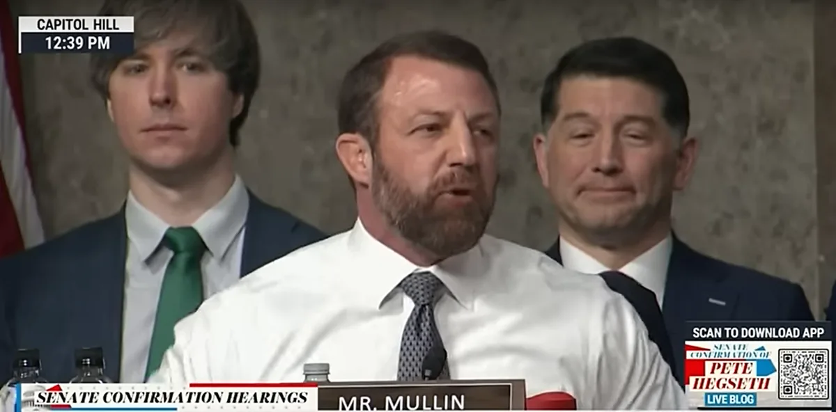 A man with a beard wearing a white shirt and tie is speaking at a podium labeled 'MR. MULLIN' during Senate confirmation…