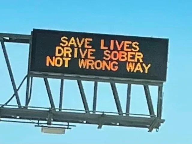 An electronic highway sign displays the message 'SAVE LIVES DRIVE SOBER NOT WRONG WAY' in orange letters against a black…