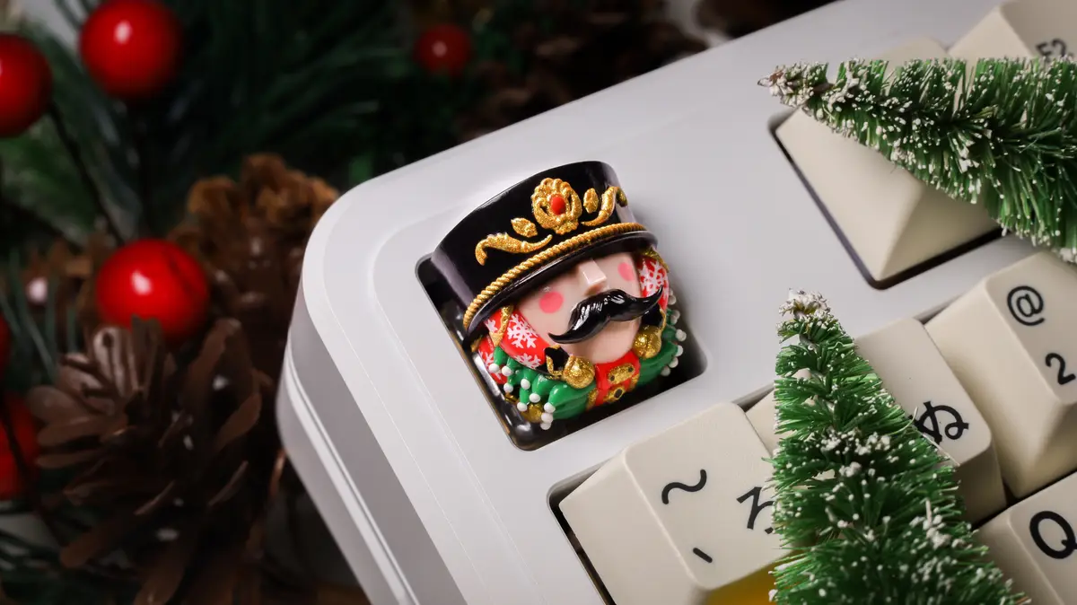 A close-up of a computer keyboard with a festive nutcracker figurine as the keycap, surrounded by miniature Christmas trees…