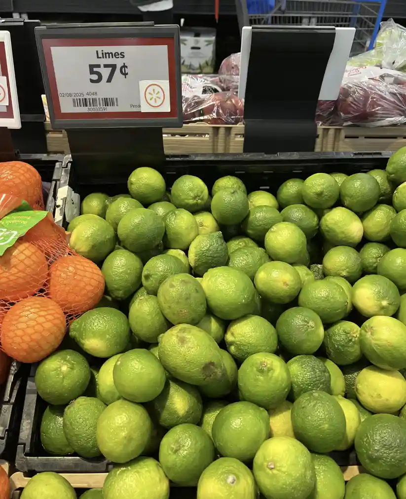A grocery store produce display shows a large bin of green limes with a price tag above reading 'Limes 57¢' and a Walmart…