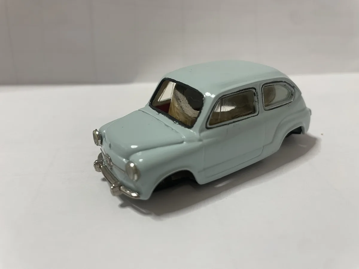 A light blue vintage toy car with a visibly broken roof and missing interior, sitting on a plain white surface. The overlaid…